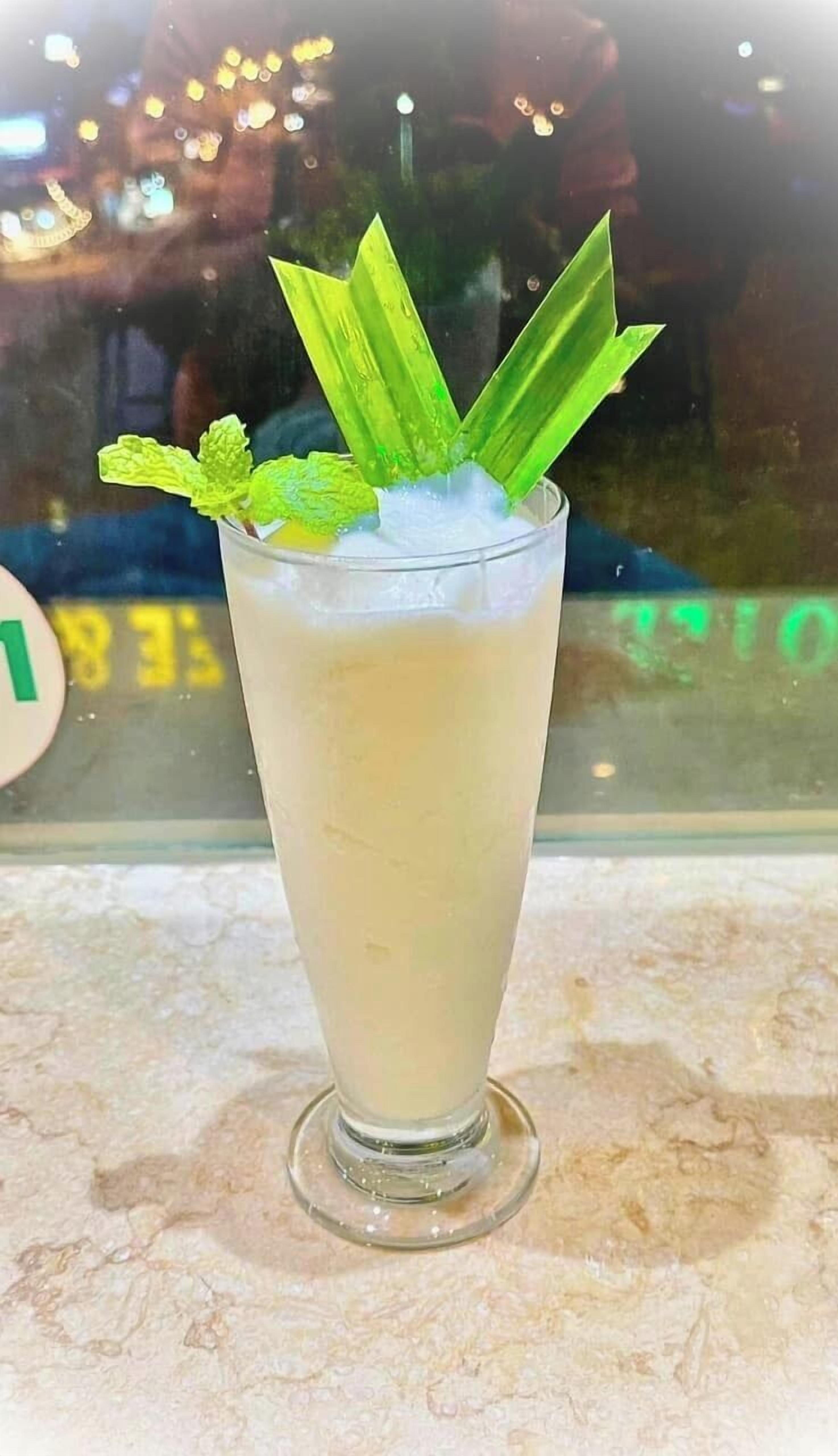 A tall glass with a beverage, garnished with mint leaves and ice cubes.
