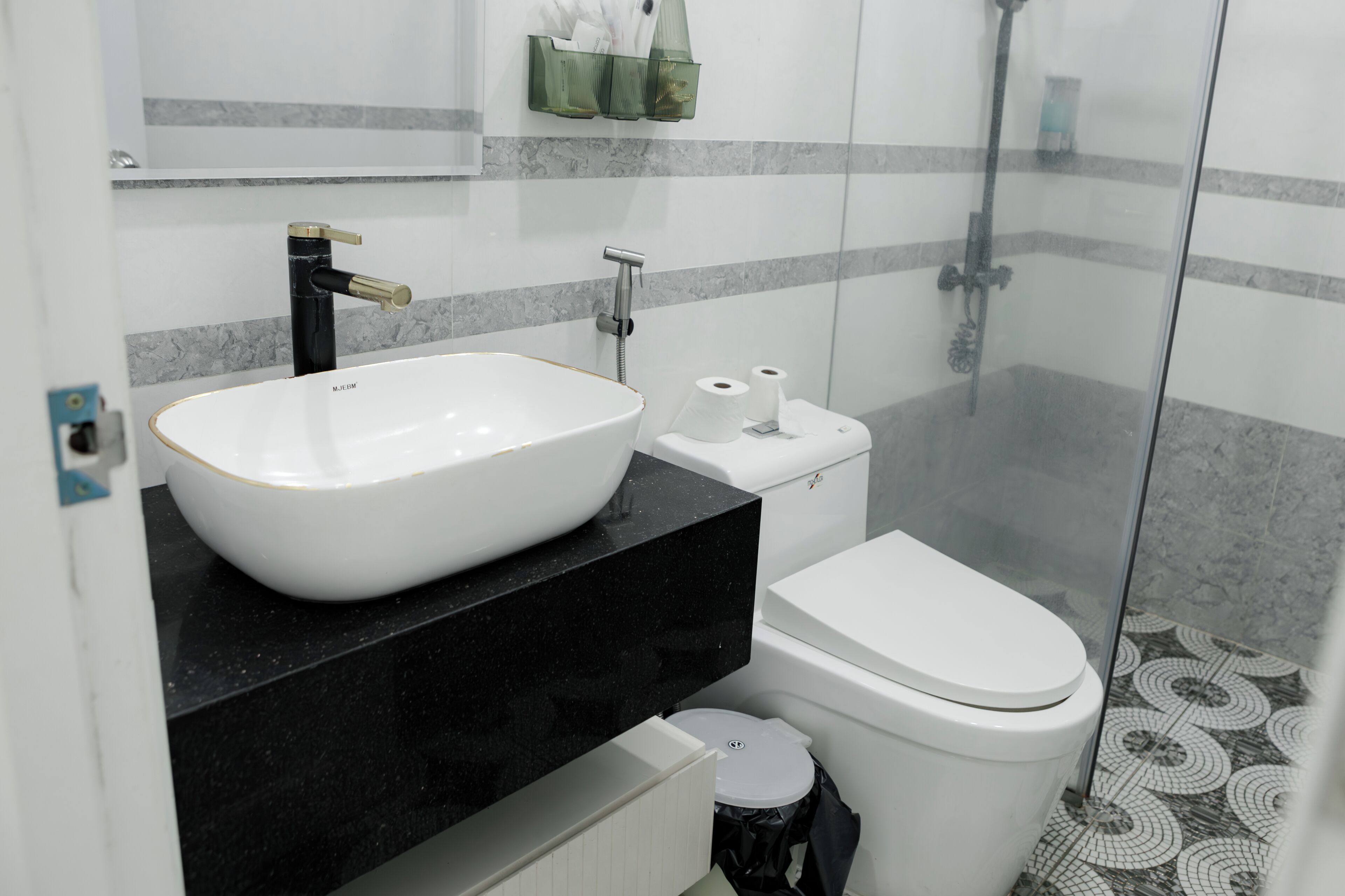 A modern bathroom with a white sink, black countertop, toilet, and a glass shower enclosure.