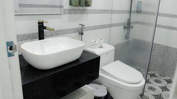A modern bathroom with a white sink, black countertop, toilet, and a glass shower enclosure.