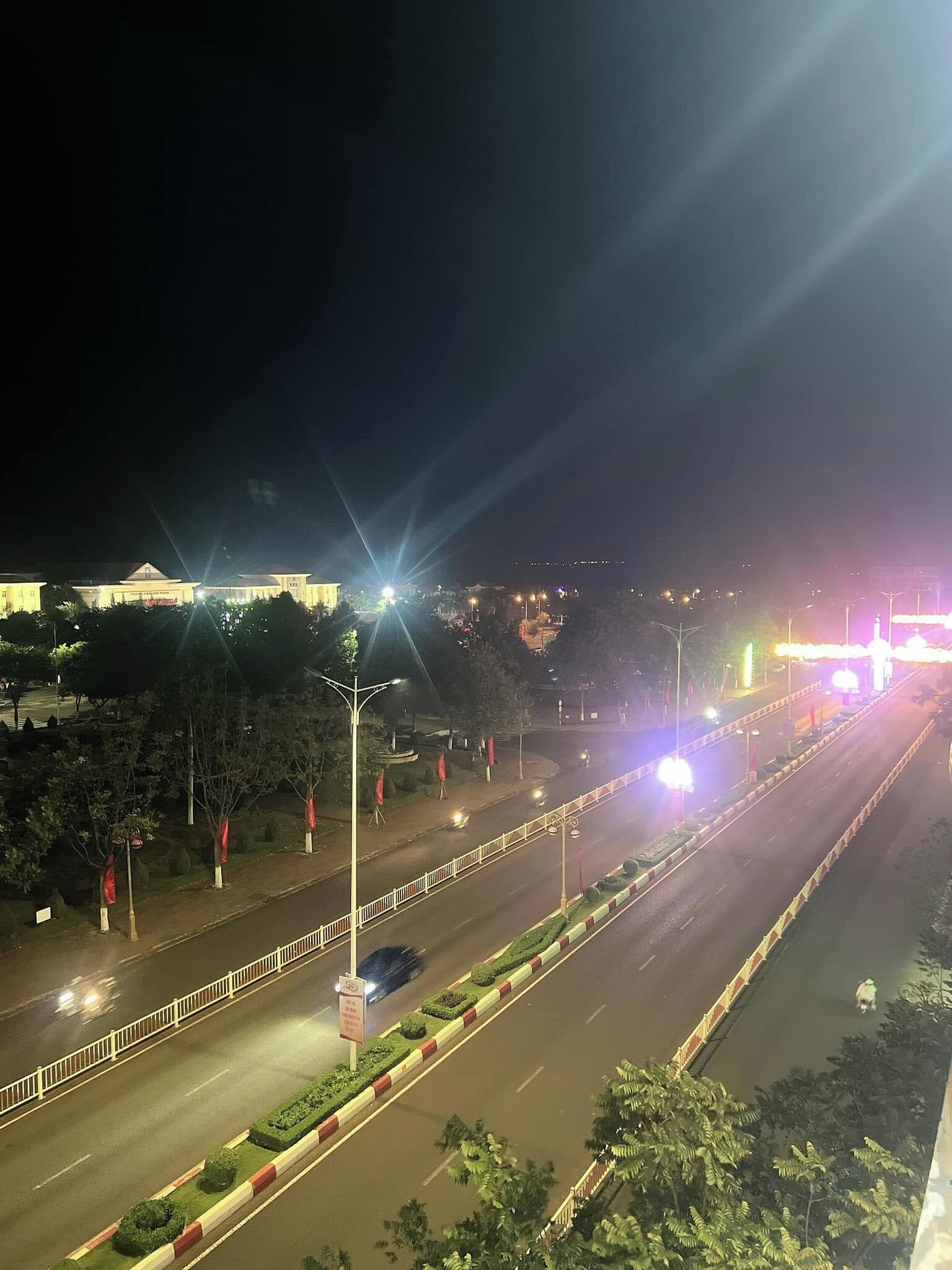 A nighttime view of a well-lit road with a clear road layout, streetlights, and a distant building.