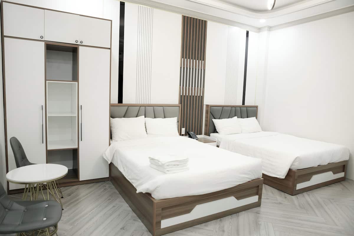 Une chambre d’hôtel moderne avec deux lits, une armoire, une petite table et une chaise.