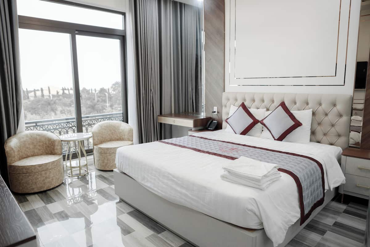 Une chambre d’hôtel moderne dotée d’un grand lit, de deux fauteuils, d’une petite table et offrant une vue sur l’extérieur grâce à de grandes fenêtres.