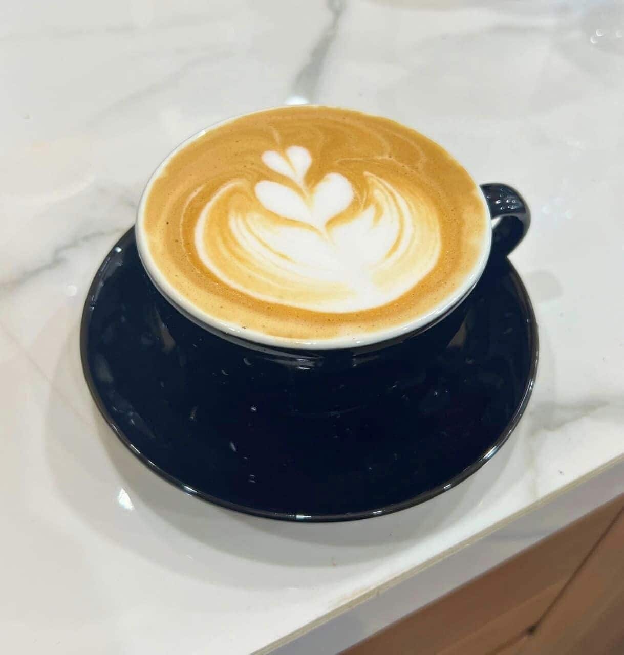 Una taza de café con arte de latte sobre un platillo negro.
