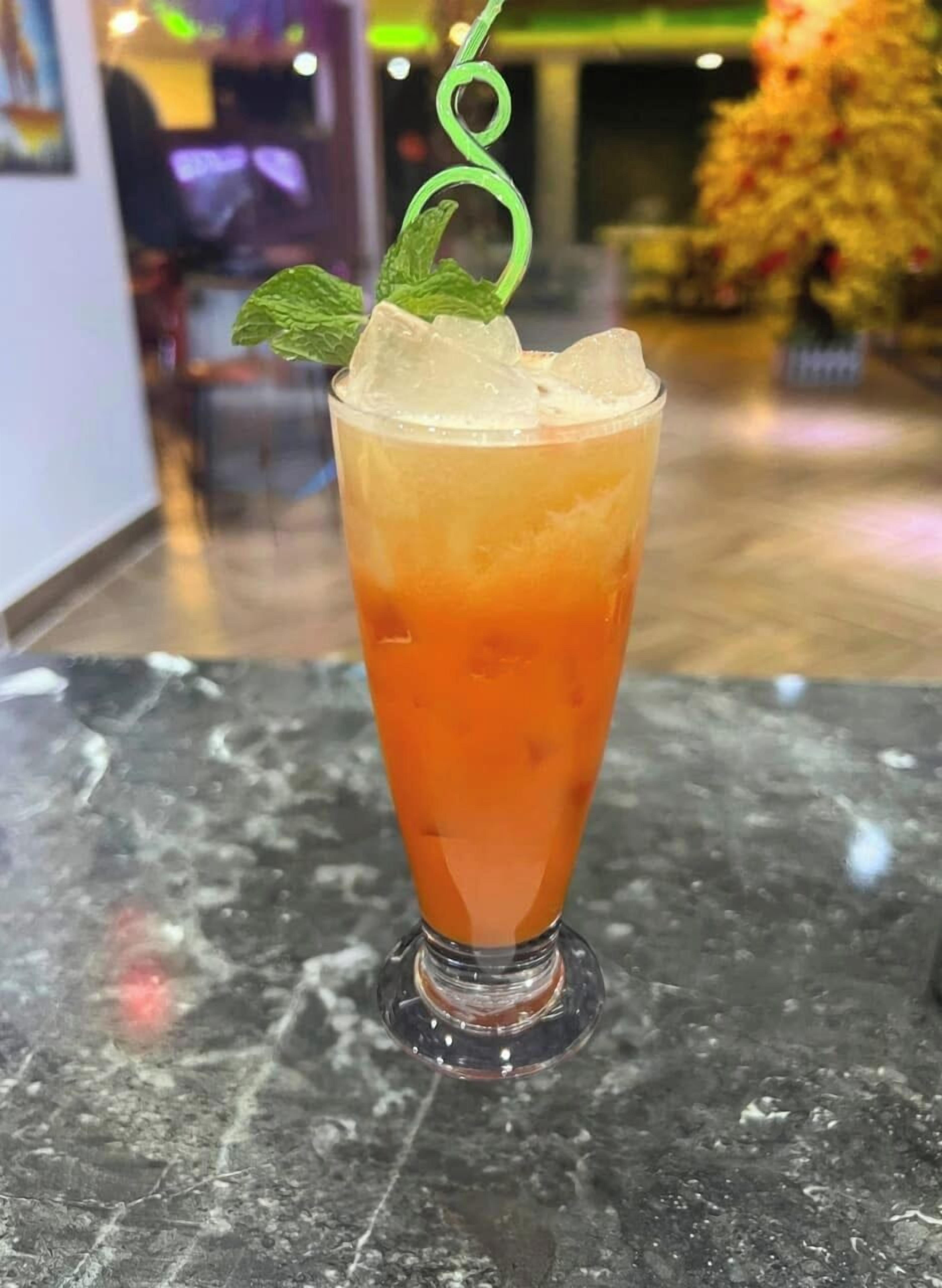A tall glass with a layered drink, ice cubes, and a mint garnish on a marble surface.