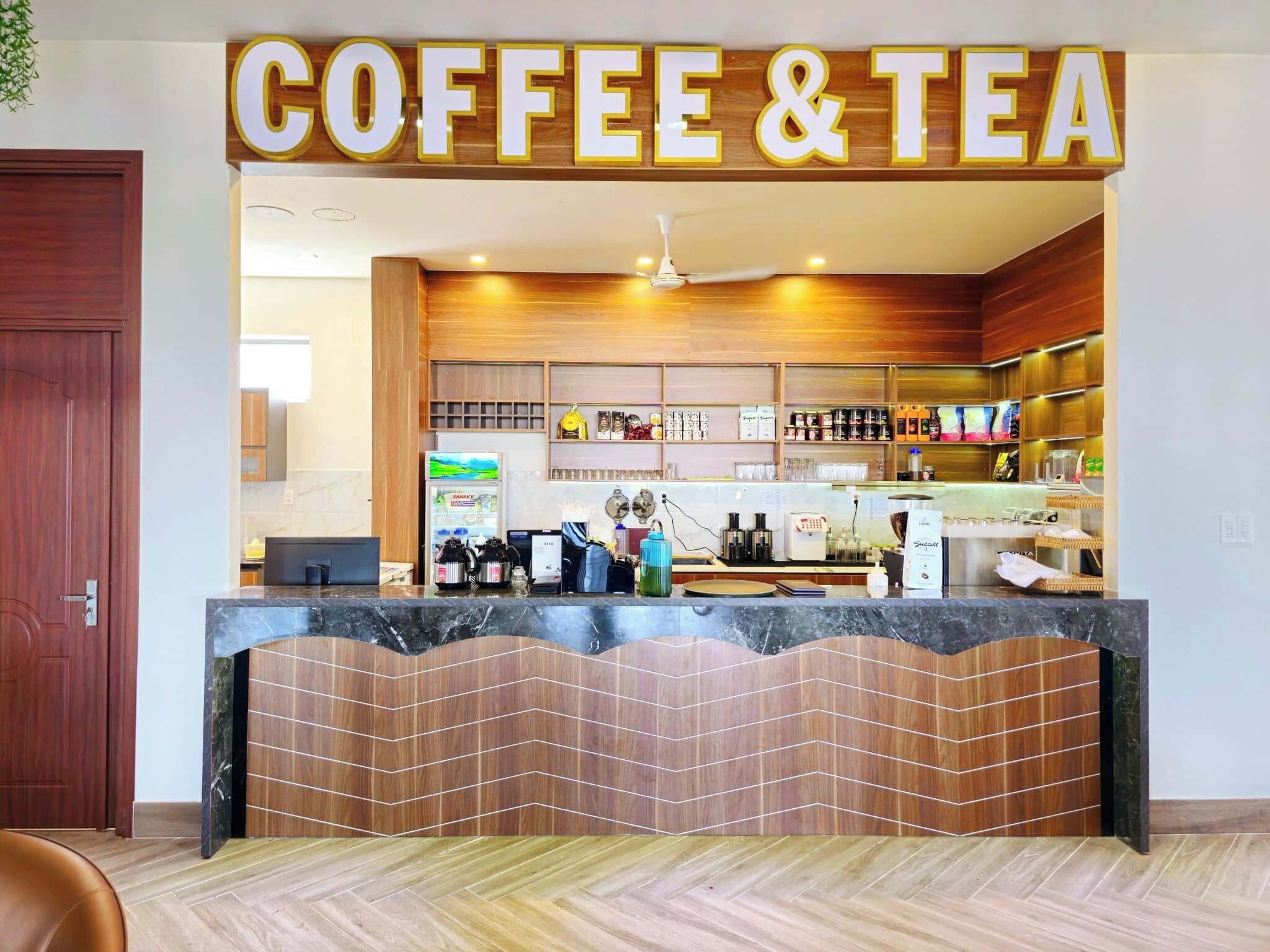 Un café-salon de thé doté d’un comptoir en bois, d’étagères remplies de divers articles et d’un décor intérieur moderne.