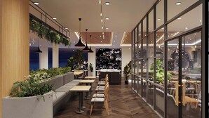 Un espacio interior moderno con una larga zona de asientos tipo banco, mesas y plantas colgantes.