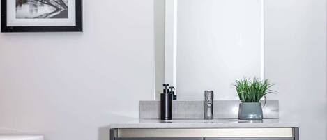 Un baño con un inodoro blanco, un mueble gris oscuro con un espejo arriba y una fotografía blanco y negro enmarcada en la pared.