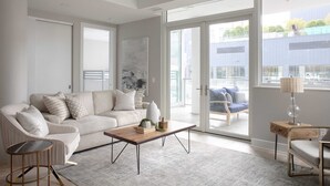 Un salon moderne avec un canapé, une table basse et une table d’appoint, de grandes fenêtres et une vue sur l’extérieur.