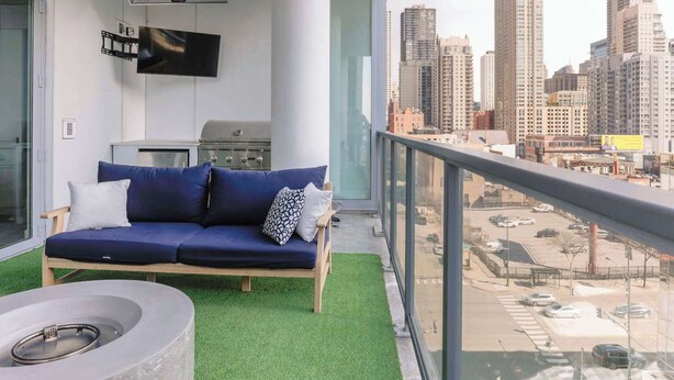 Un balcon avec un canapé bleu, un petit barbecue et un téléviseur.