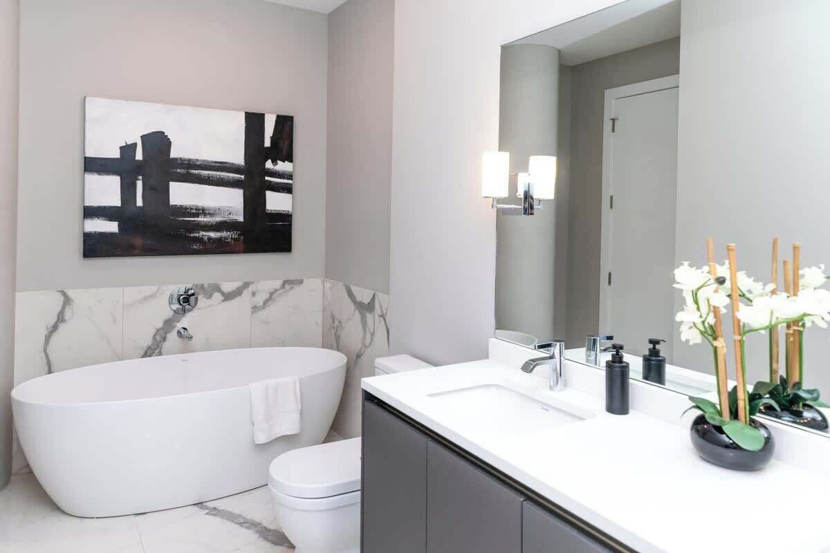 A modern bathroom with a freestanding bathtub, a toilet, a vanity with a mirror, and a wall-mounted light fixture.
