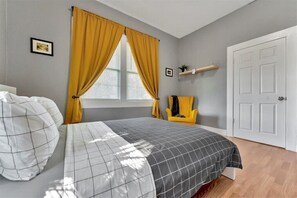 Une chambre à coucher comprenant un lit, une chaise, une fenêtre avec des rideaux, une porte et une étagère avec divers objets.