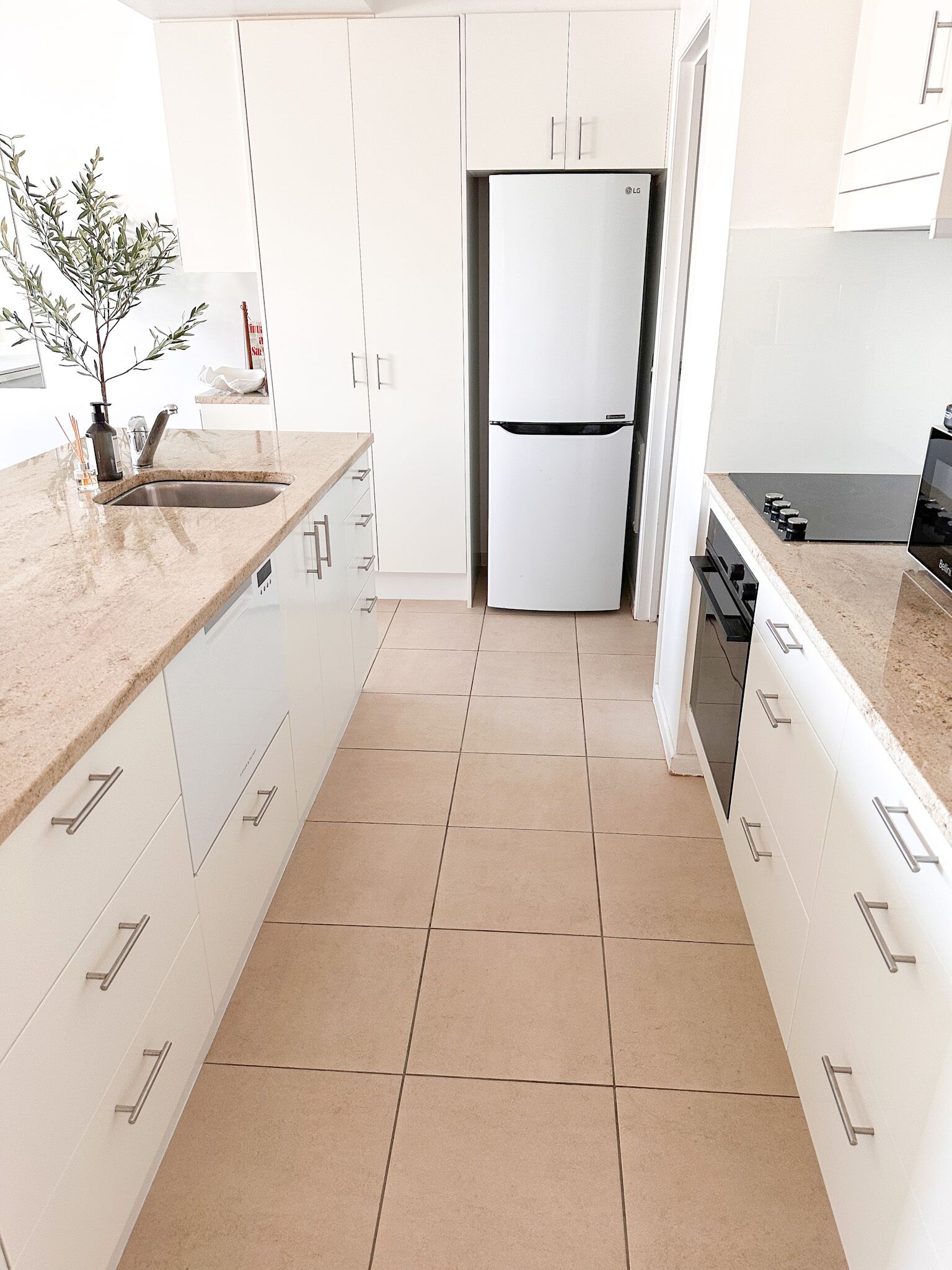 Een moderne keuken met witte kasten, een koel-vriescombinatie en een betegelde vloer.
