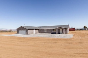 Un bâtiment d’un seul étage, doté d’un garage, d’une allée couverte et d’un terrain en terre battue au premier plan.