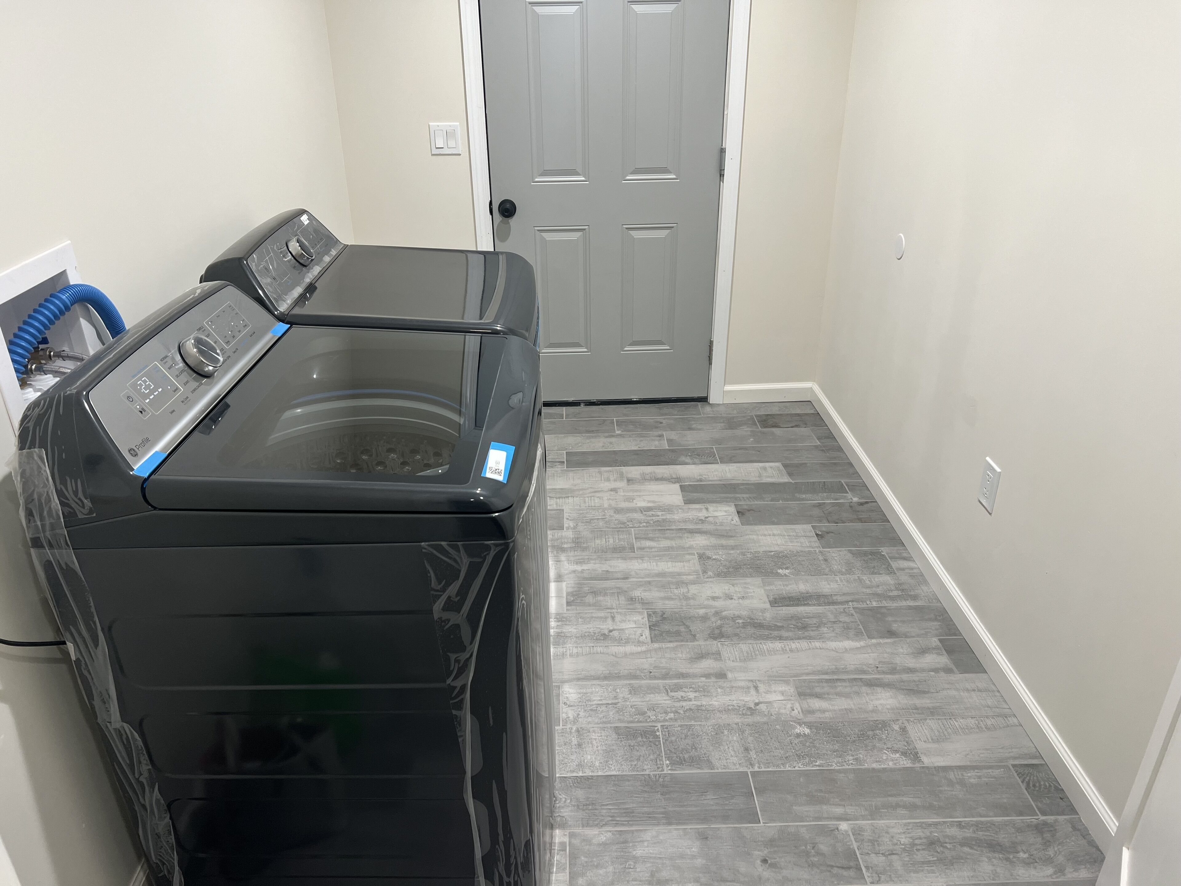 A laundry room with a black washer and dryer, grey herringbone-patterned flooring, and a white door.