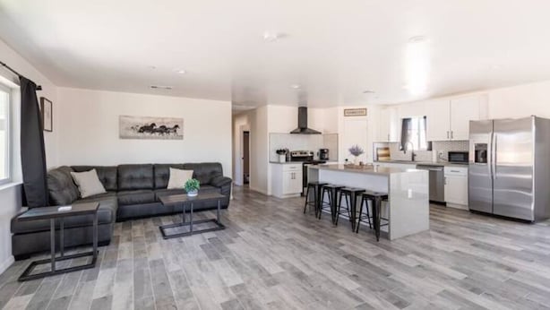 Un salon moderne avec un canapé d’angle, une table basse et un coin repas, la cuisine étant visible au fond.