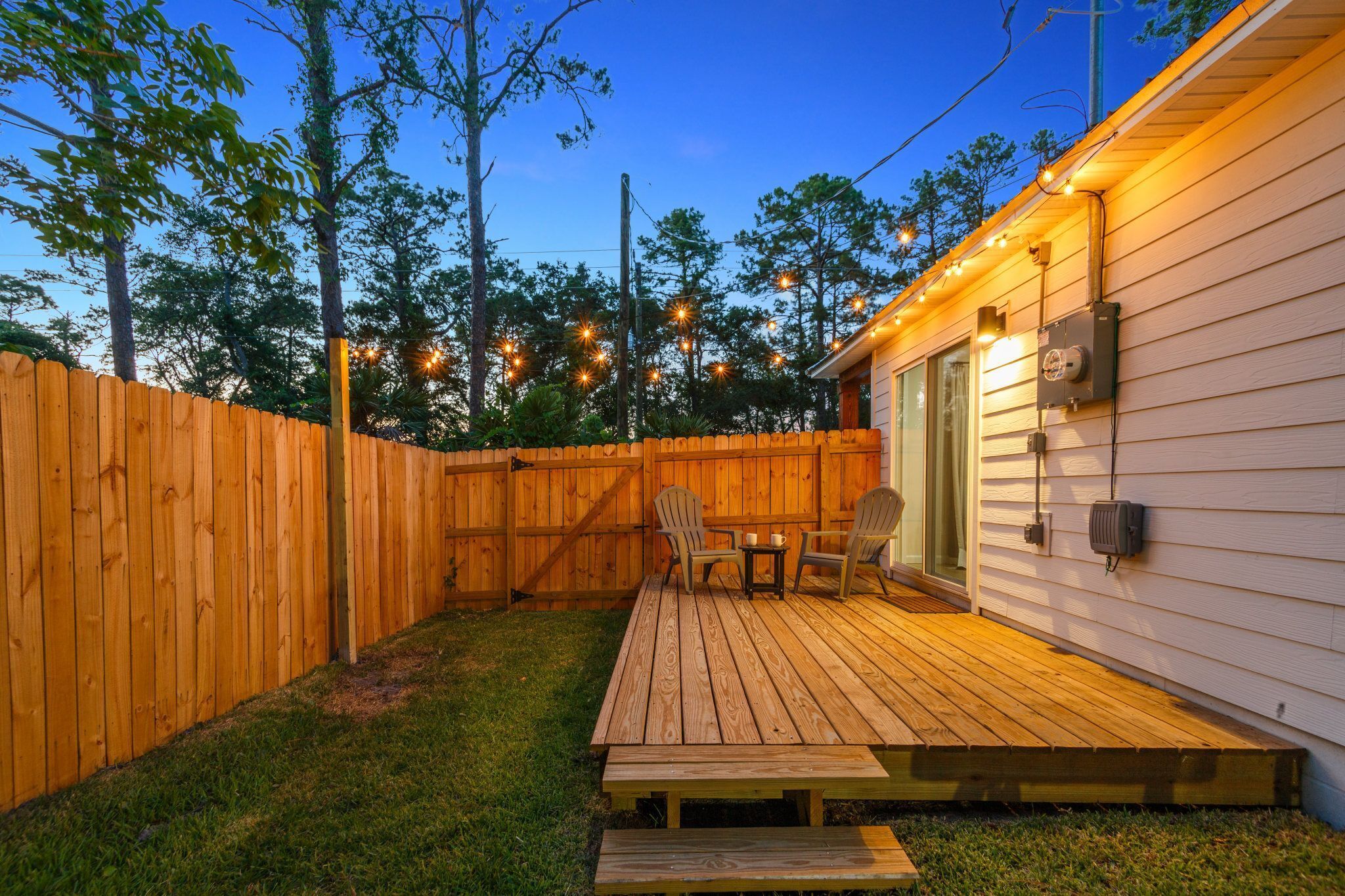 Un jardin avec une terrasse en bois, deux chaises et une table.
