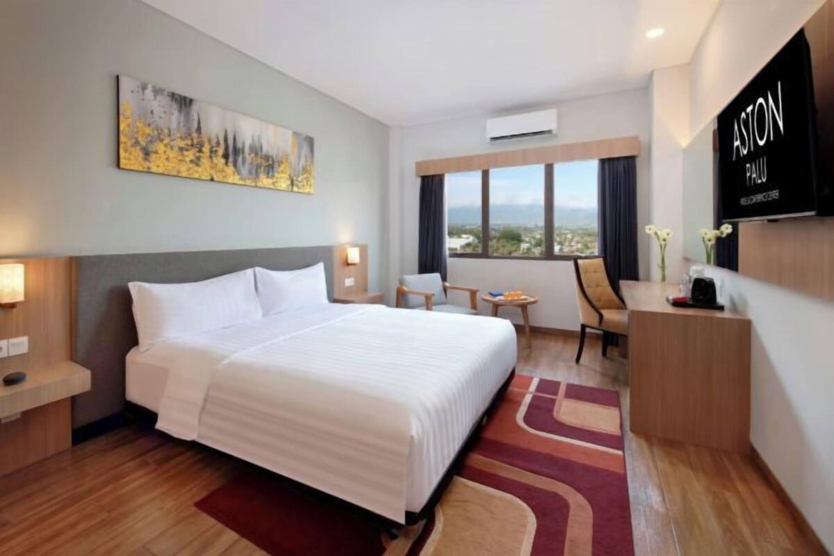 A hotel room with a large bed, a desk, a chair, a TV, and a painting on the wall.