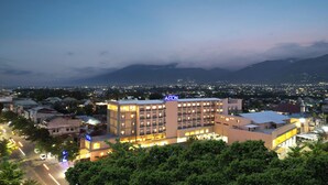 A multi-story hotel with a prominent 'ASTON' sign, surrounded by lush greenery and a view of a cityscape with mountains in the background. - Aston Palu Hotel & Conference Center (Palu)