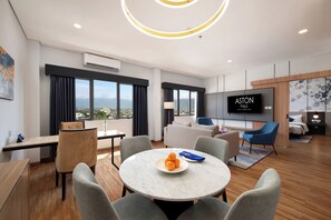 A modern hotel room with a dining area, a living area with a TV, and a view of the city. - Aston Palu Hotel & Conference Center (Palu)