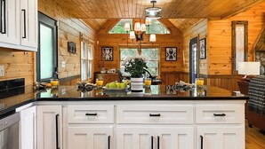 A wooden cabin interior with a kitchen featuring a large island, white cabinetry, and a dining area with a brown leather couch. - Amazing Overlook Mtn Cabin Near DT Blue Ridge (Blue Ridge)