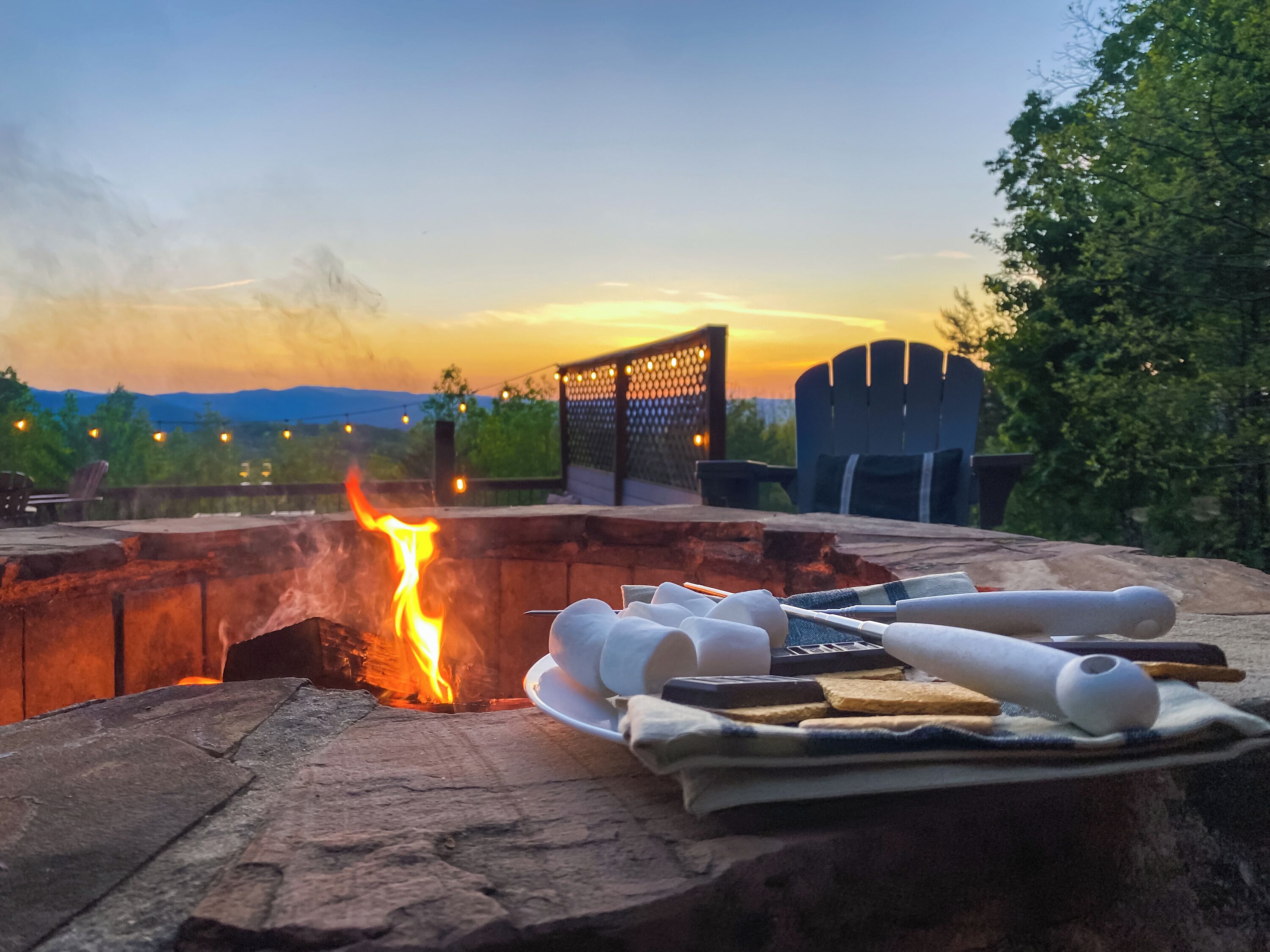 Un feu de camp avec des guimauves et une assiette de nourriture, entouré de chaises et d’une clôture.