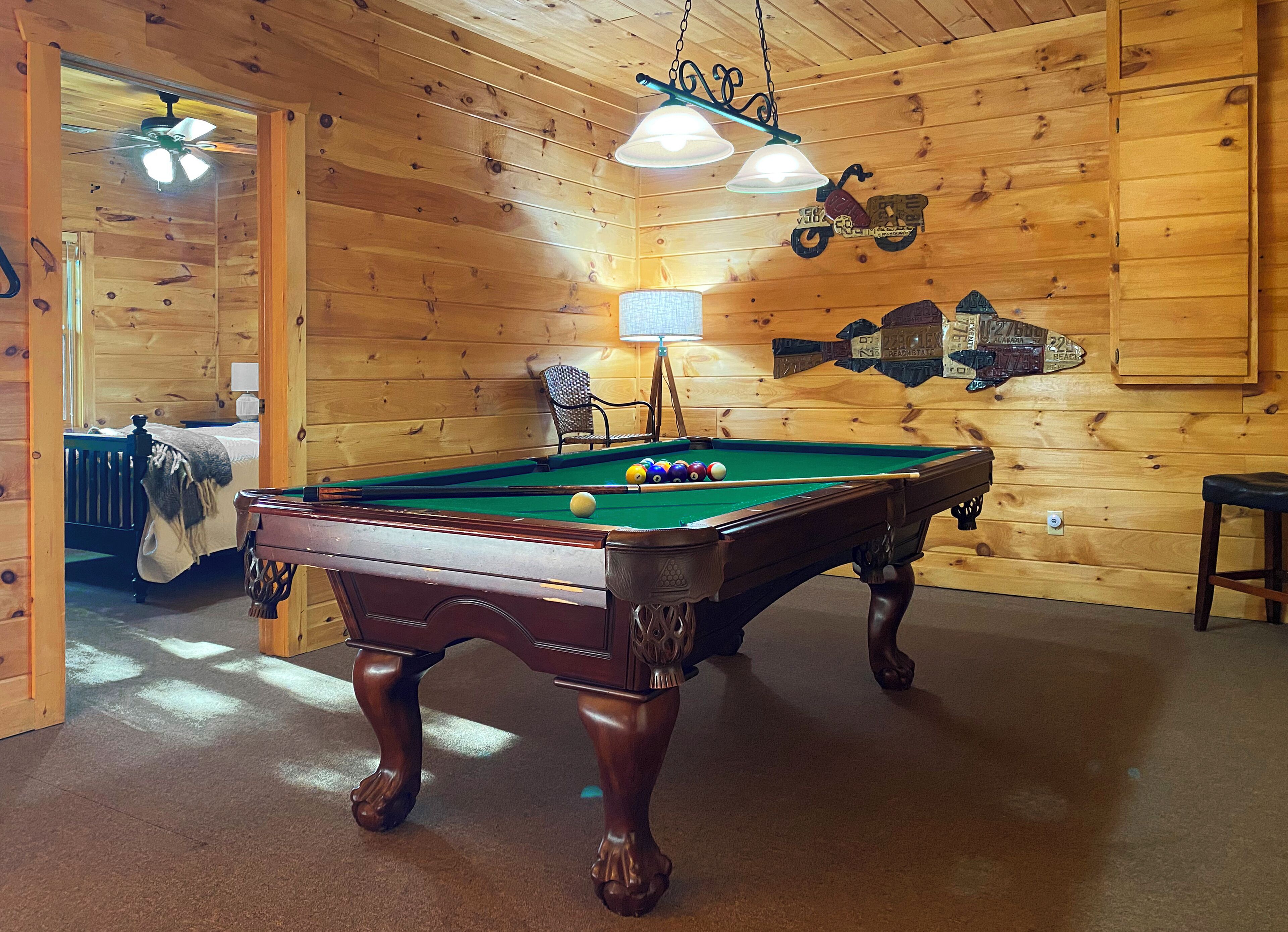 A pool table in a room with wooden walls, a ceiling fan, and a lamp.