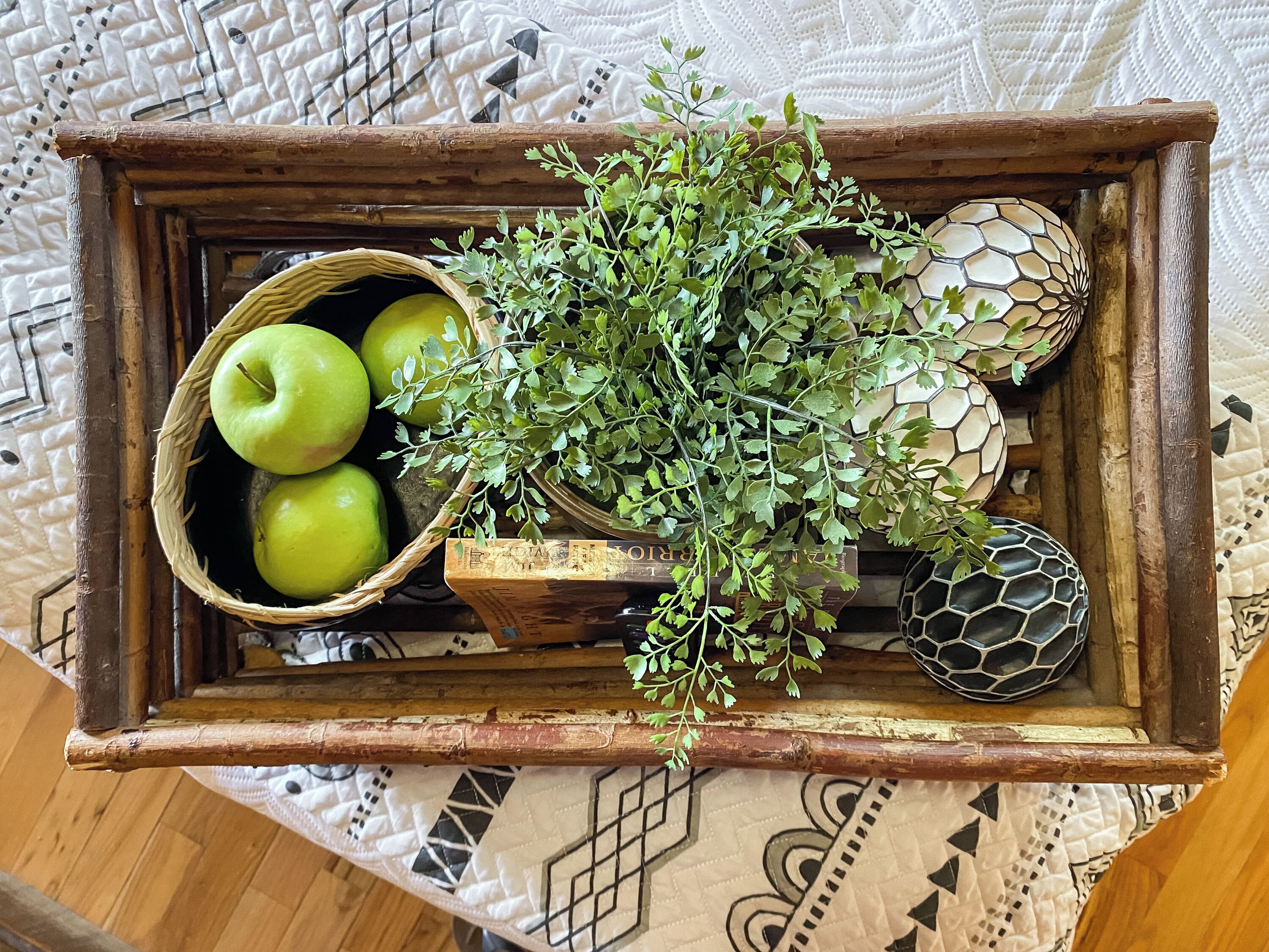 Een houten dienblad met een gevlochten mandje met groene appels, een takje groen en decoratieve eieren.