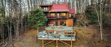 A log cabin with a red roof, a deck with outdoor seating, and a forested backdrop.