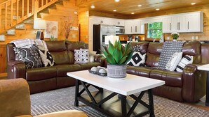 A cozy living room with a brown leather sofa, a white coffee table, and a potted plant. A staircase with wooden railings leads to an upper level. - Amazing Overlook Mtn Cabin Near DT Blue Ridge (Blue Ridge)