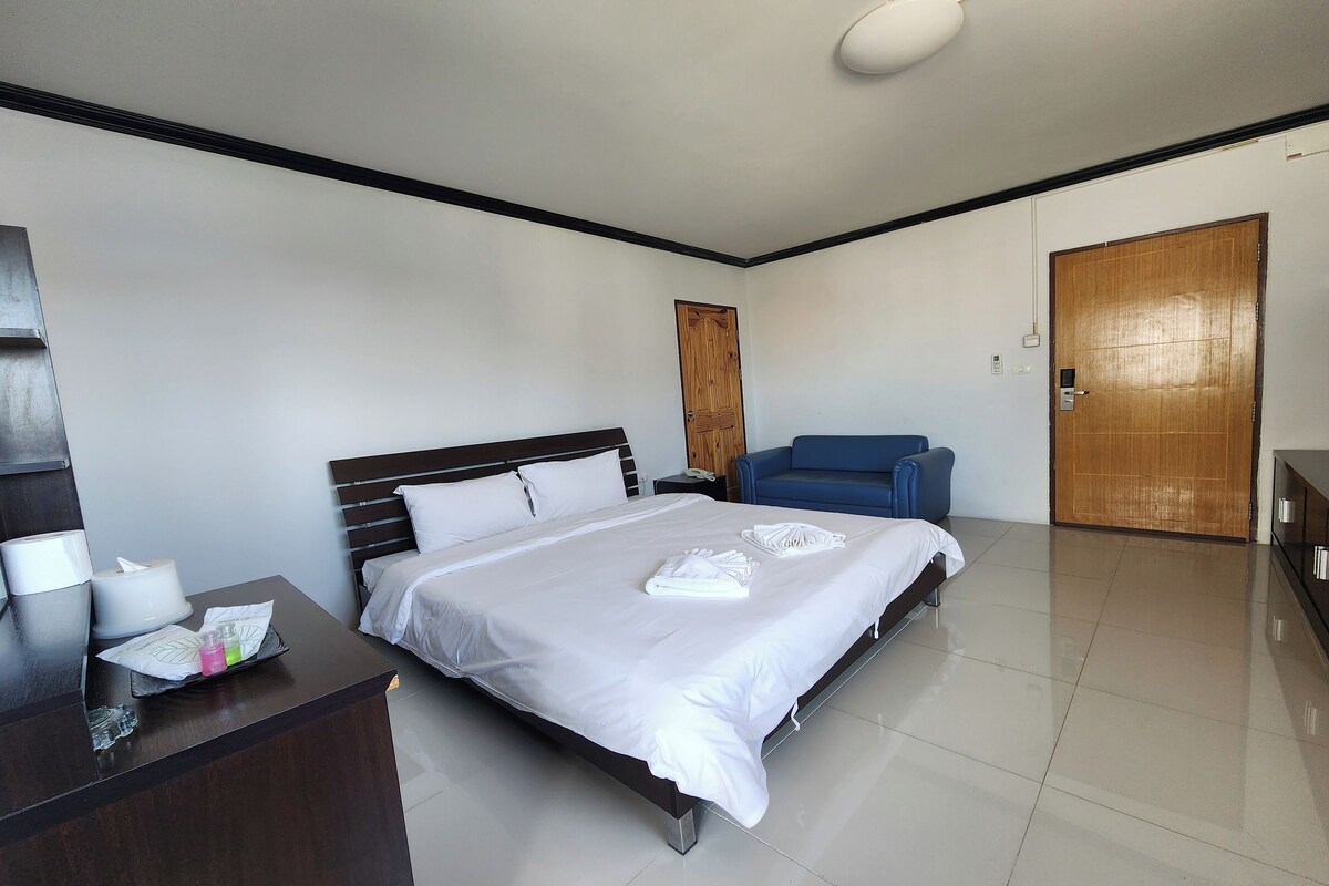 A hotel room with a large bed, a desk with a lamp, a chair, and a wooden door.