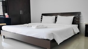 A modern bedroom with a large bed, dark wooden headboard, and white bedding. - One Residence (Khlong Luang)