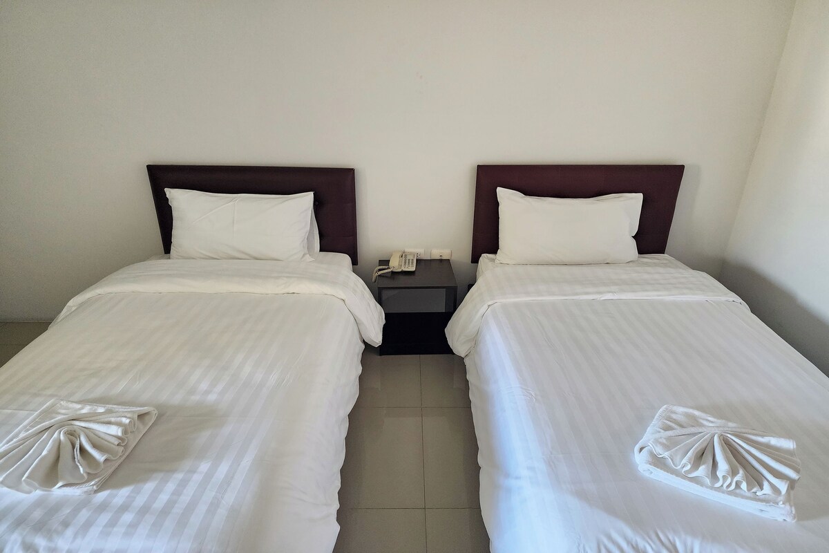 A hotel room with two single beds, each with a white bedspread and pillows, and a small bedside table with a telephone.