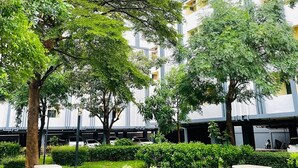A courtyard with trees, benches, and a multi-story building with balconies. - One Residence (Khlong Luang)