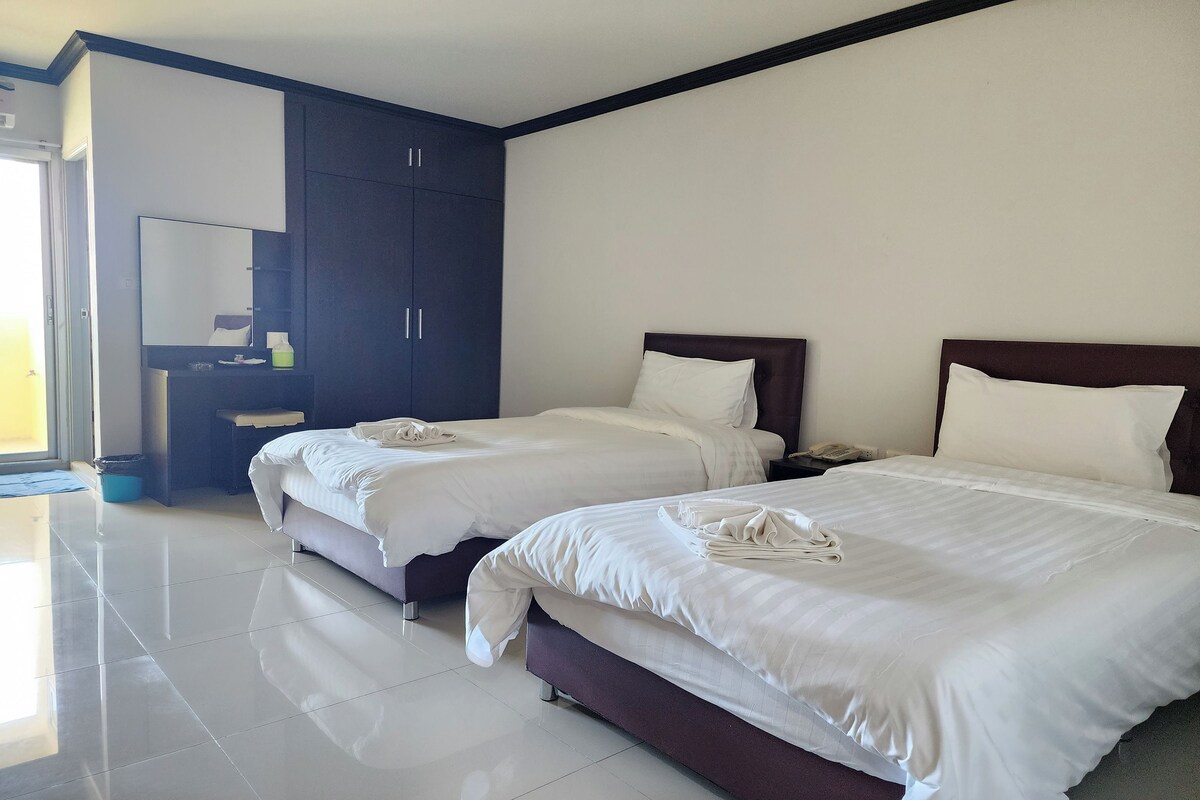A hotel room with two beds, a large wardrobe, and a bathroom area.