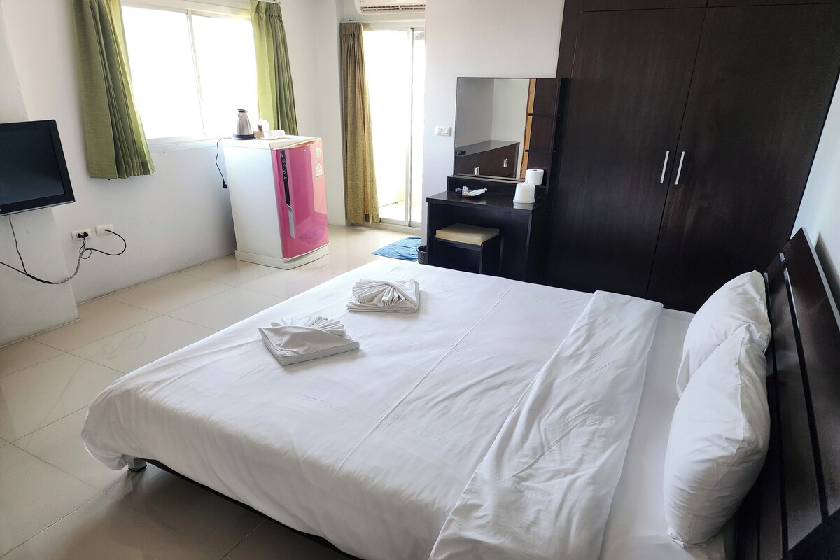 A hotel room with a bed, a desk, a wardrobe, a television, and a window with curtains.