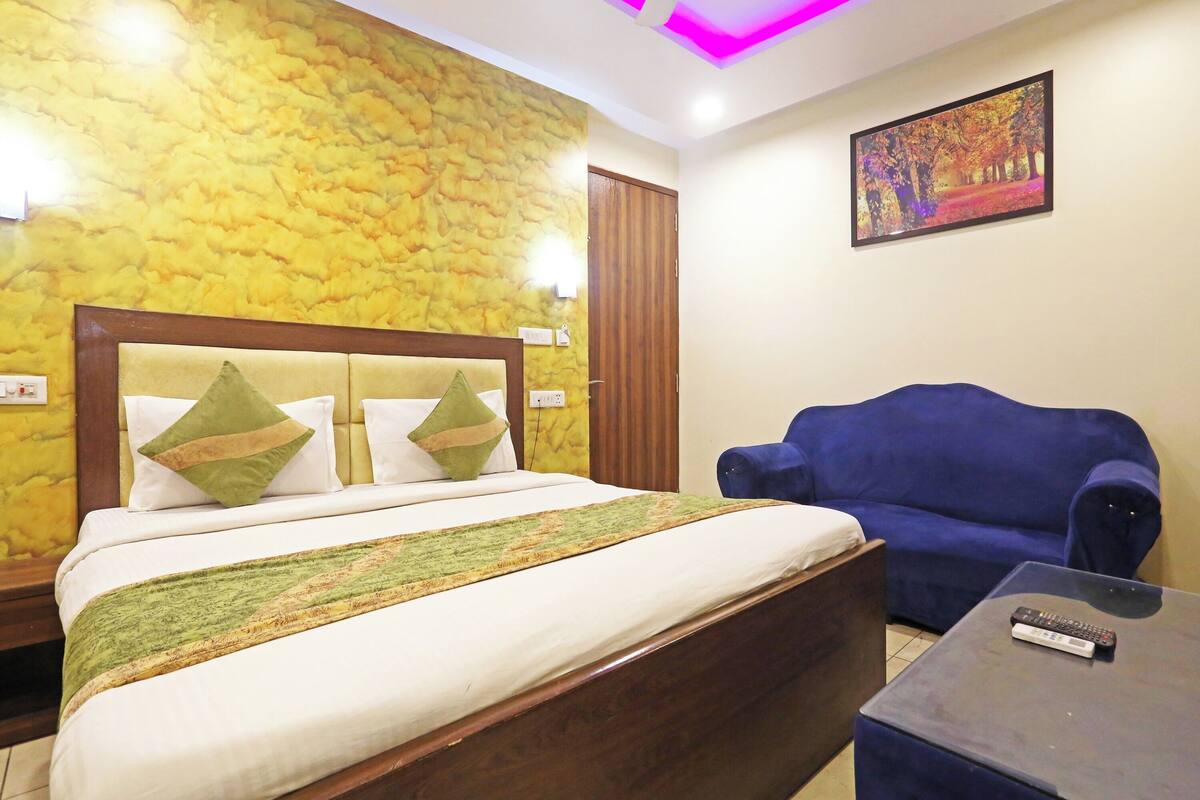 A hotel room with a bed, a blue sofa, a small table, and a painting on the wall.