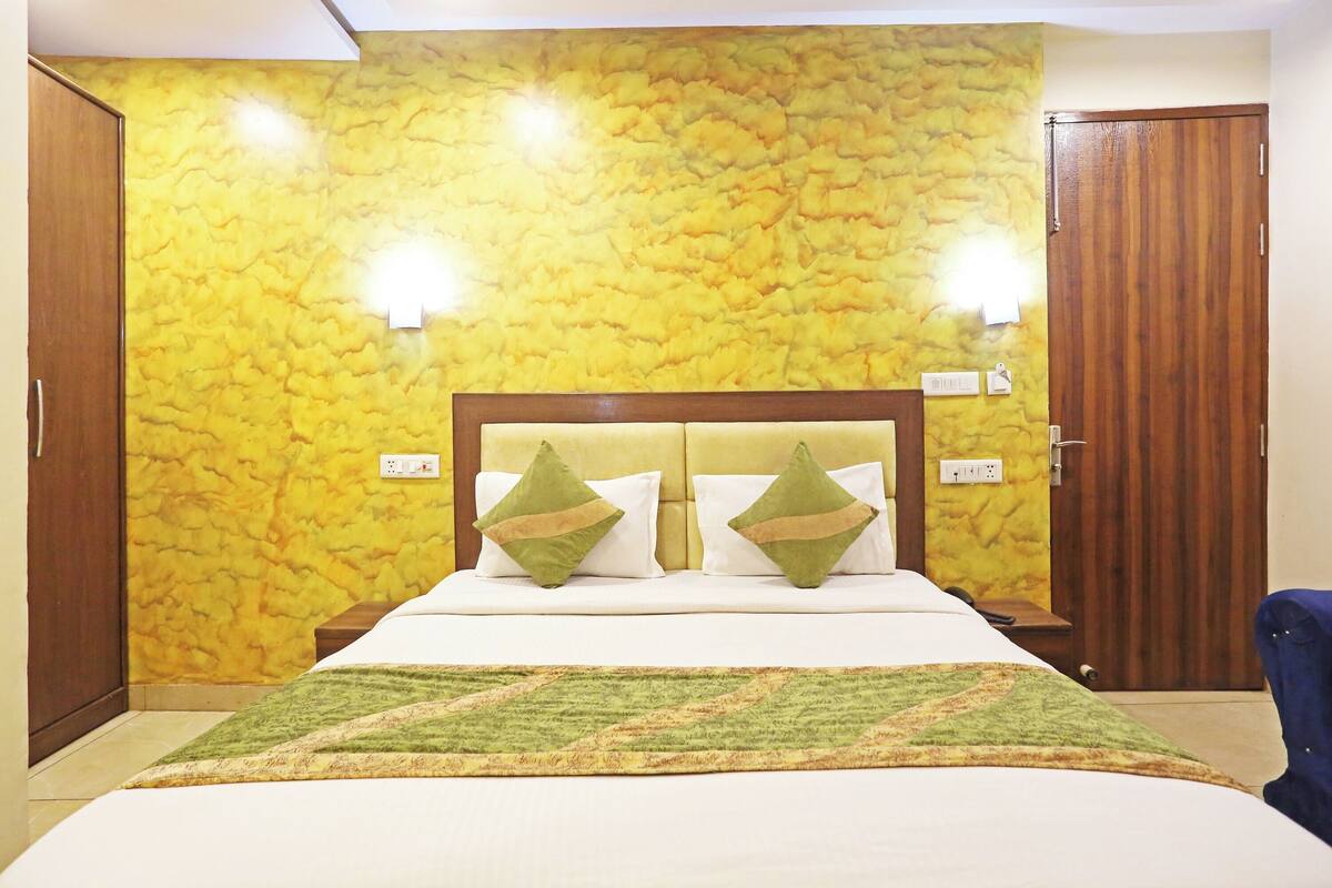 A hotel room with a bed, two bedside lamps, a wooden wardrobe, and a textured yellow wall.