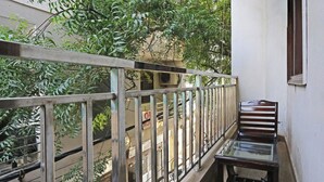 Een balkon met een metalen hekwerk, een houten bankje en uitzicht op een gebouw met een bord.