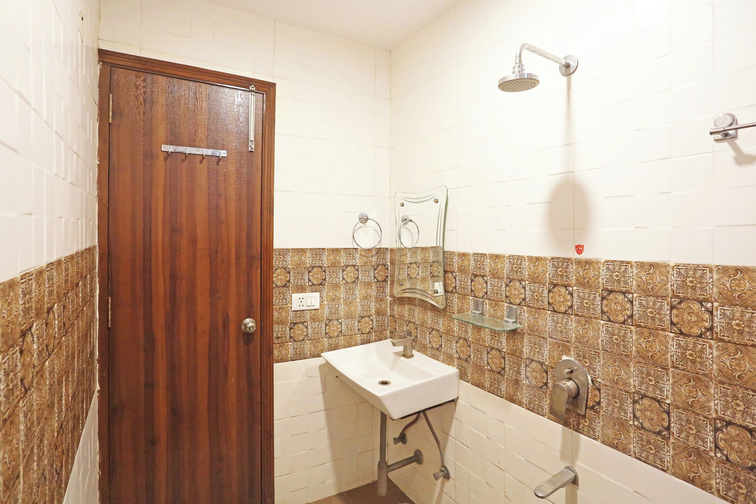 Un bagno con una porta in legno, un lavandino bianco, cabina doccia in vetro e piastrelle decorate.