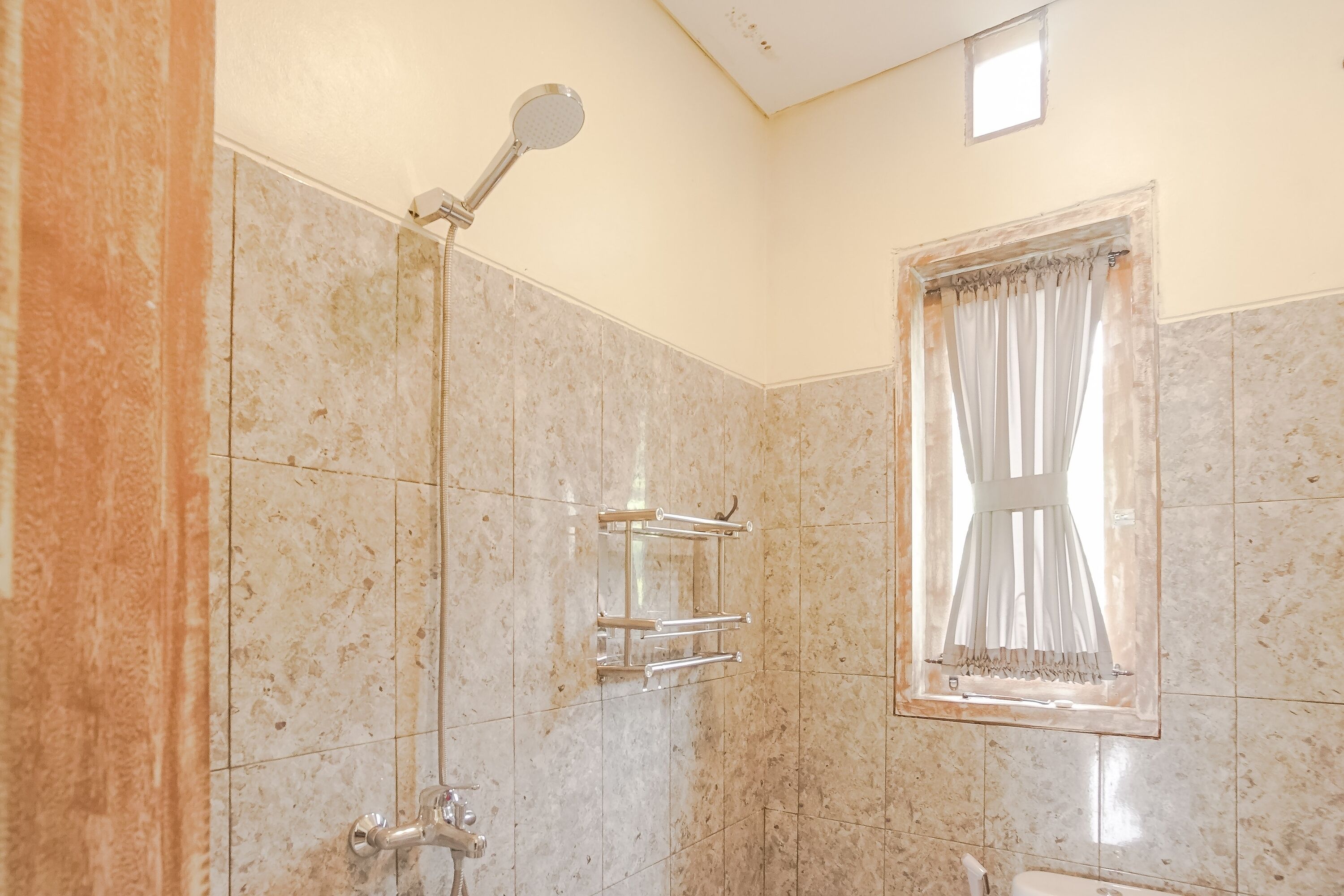 Un baño con ducha, inodoro y ventana con cortinas.