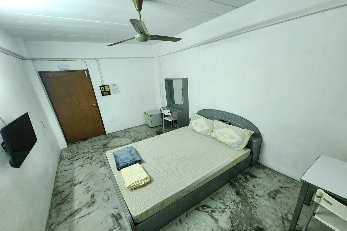 A room with a bed, a desk, a chair, a ceiling fan, and a door.