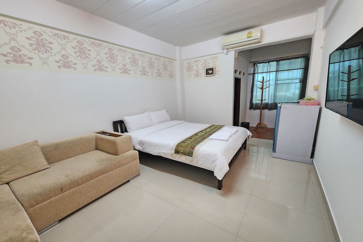 A hotel room with a bed, a sofa, a small refrigerator, and a window with curtains.