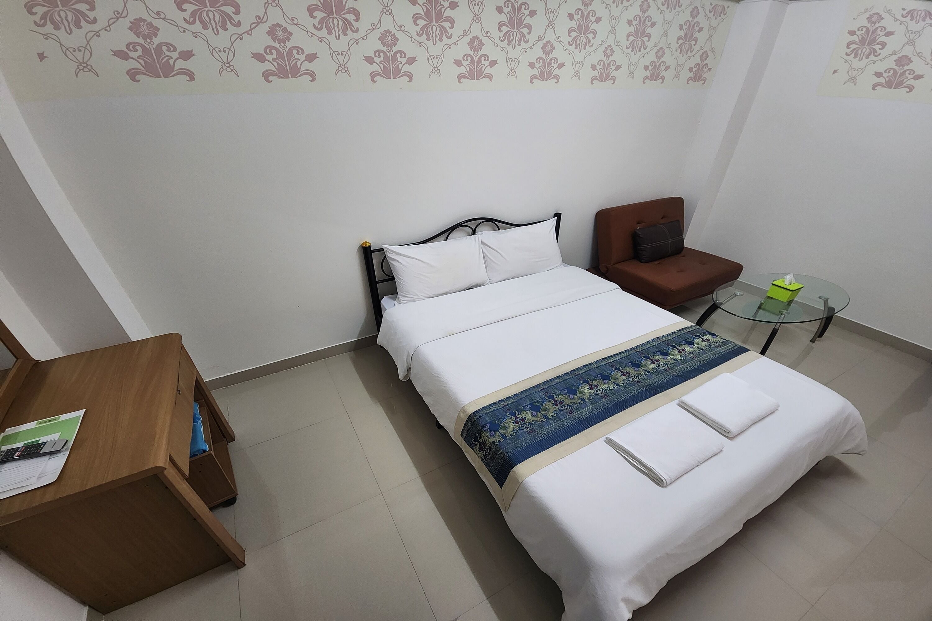 Habitación de hotel ordenada con cama, una mesita pequeña, una silla y un escritorio de madera.