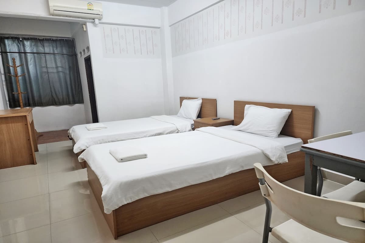 A hotel room with two single beds, a wooden desk, a chair, and a small table.