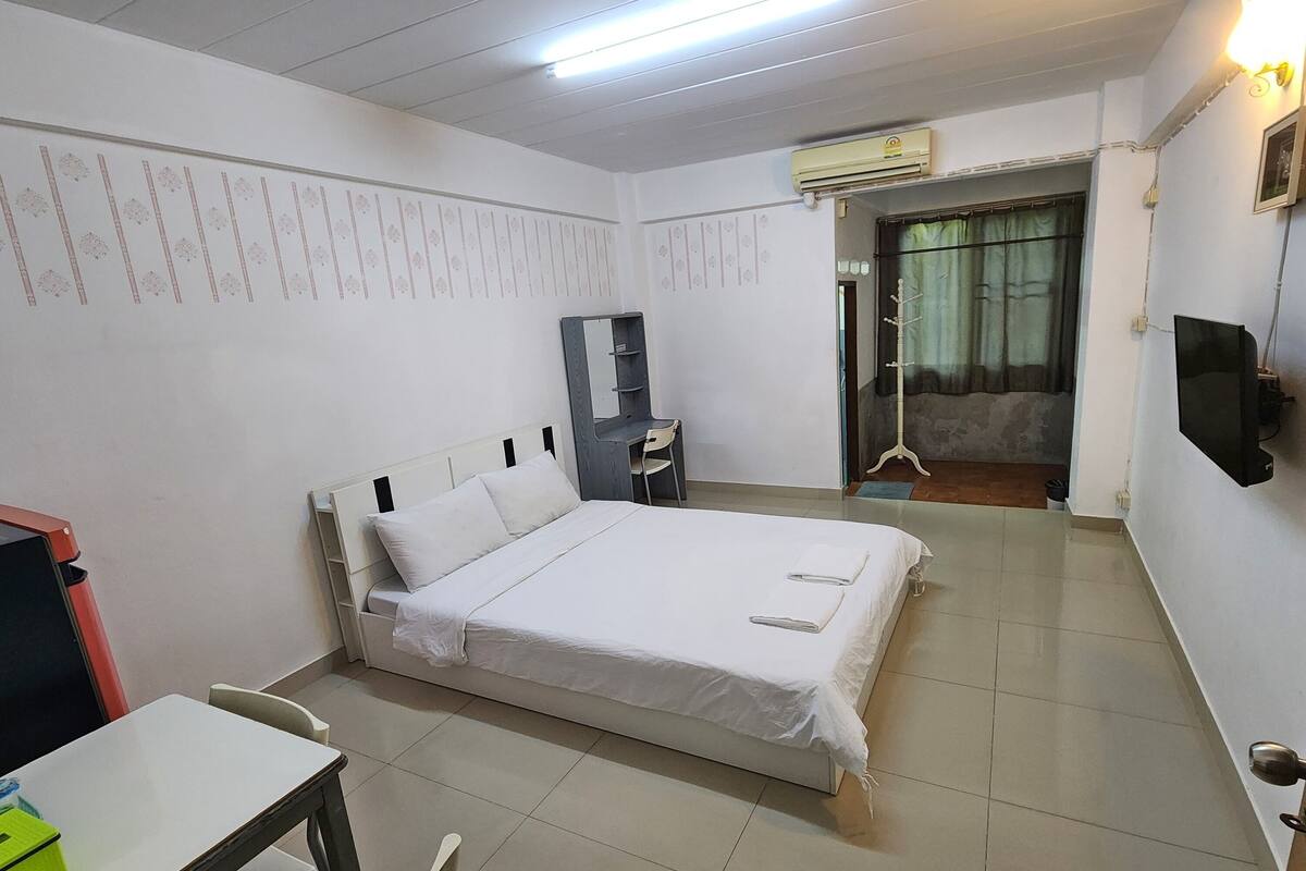 A bedroom with a bed, a desk, a chair, a mirror, and a TV.