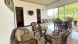 A spacious room with wicker furniture, a glass table, and a television on the wall.