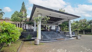 A covered entrance with steps leading up to a building, surrounded by greenery and a clear sky.