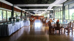 A spacious restaurant with high ceilings, large windows, and a long dining area with tables and chairs.