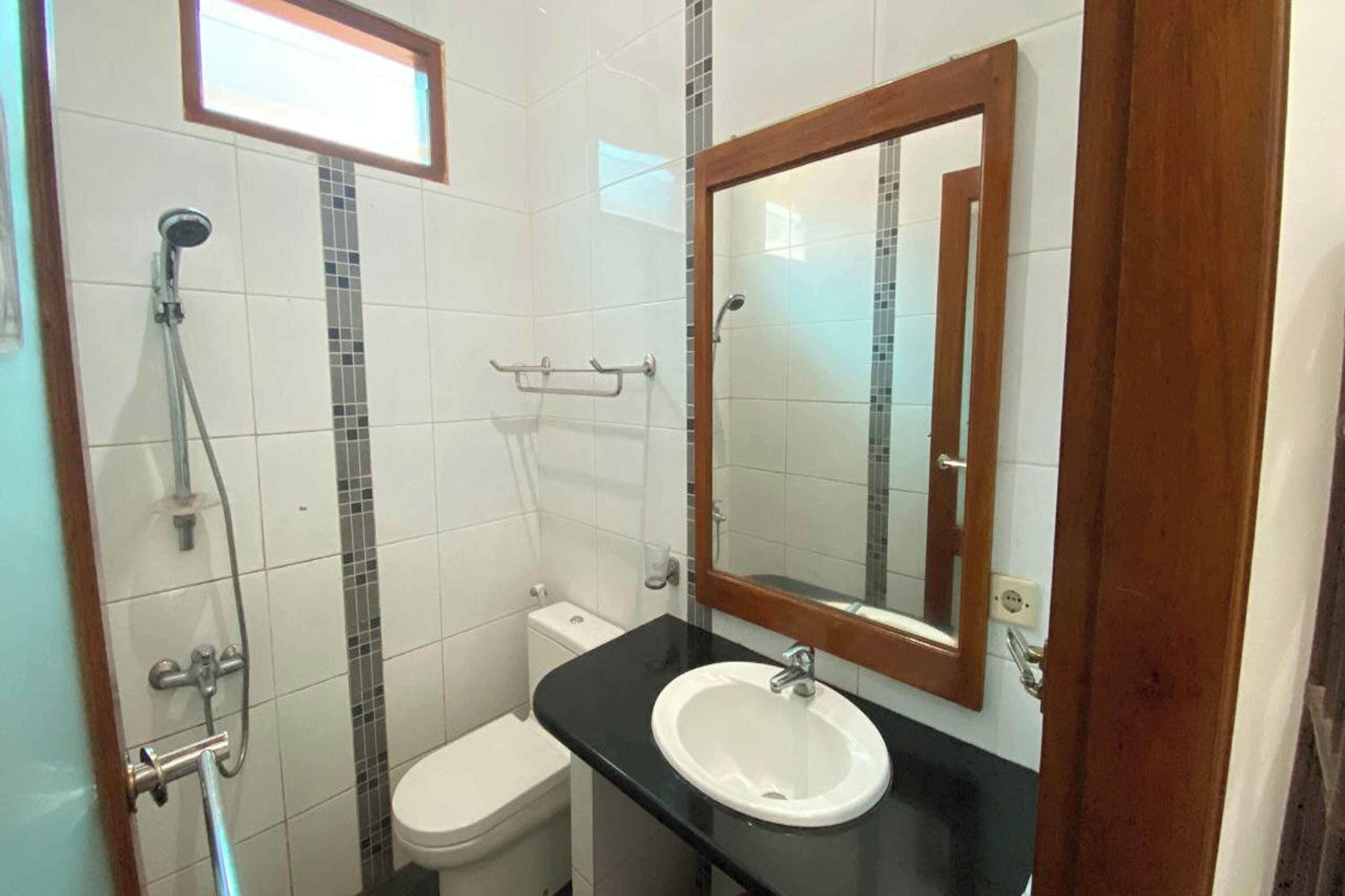 Ein Badezimmer mit Toilette in Weiß, einem schwarzen Waschbecken, einem Spiegel mit Holzrahmen und einer Dusche mit Glastür.