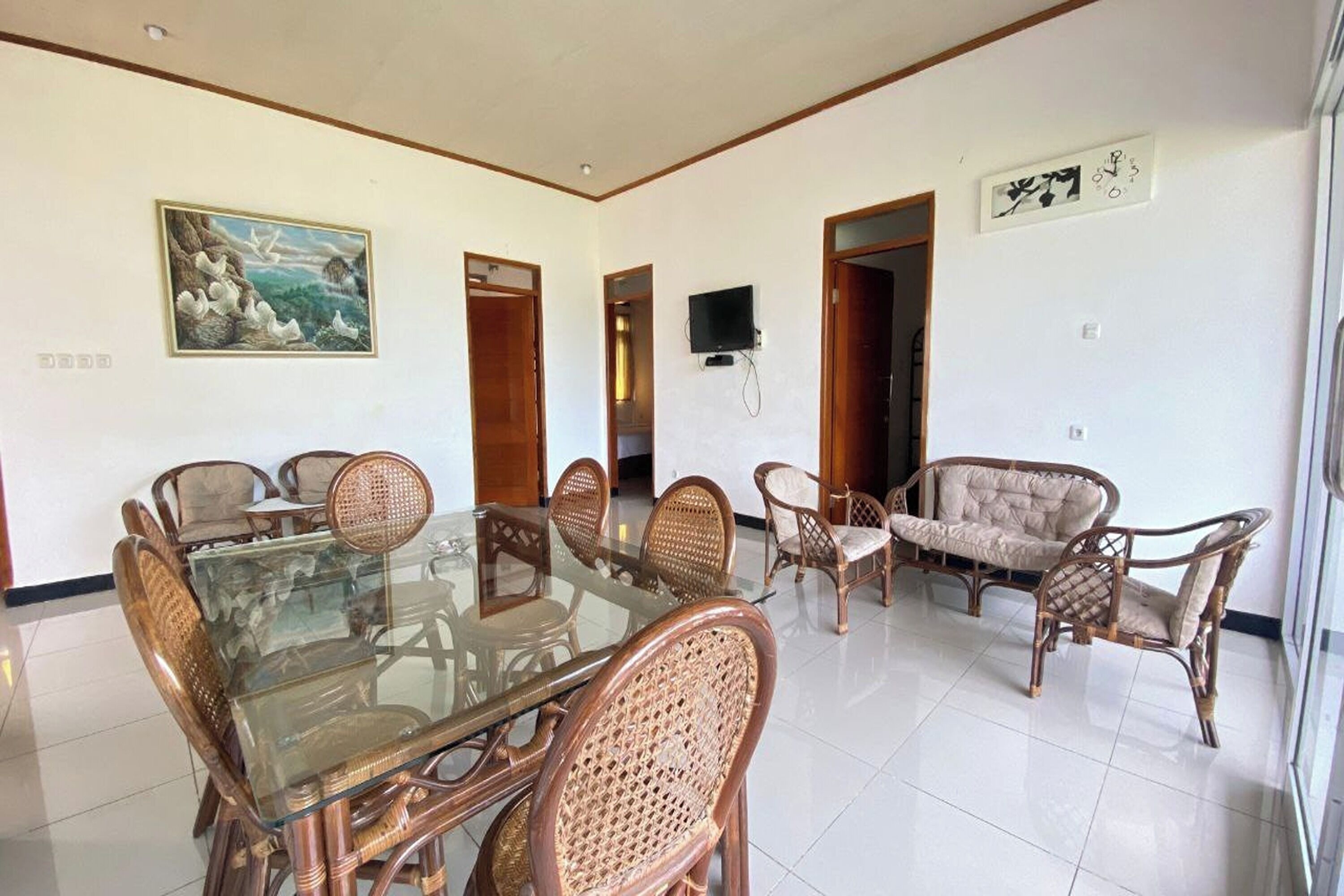 A dining area with a glass-top table surrounded by wicker chairs, a sofa, and a television mounted on the wall.